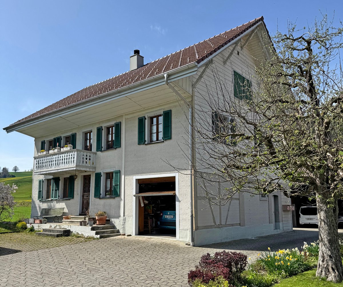 2 story house, white exterior, brown roof, balcony, garage, garden, green shutters, chimney, bench, potted plants