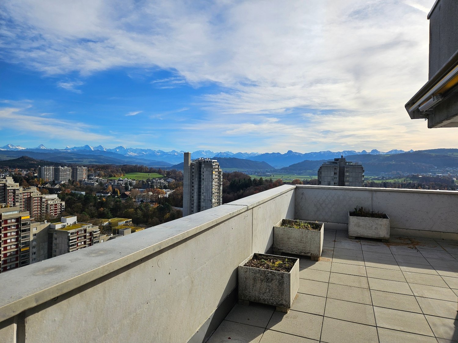 Terrace with 3 planters, tiled floor, white walls, mountain views, multiple buildings in the distance
