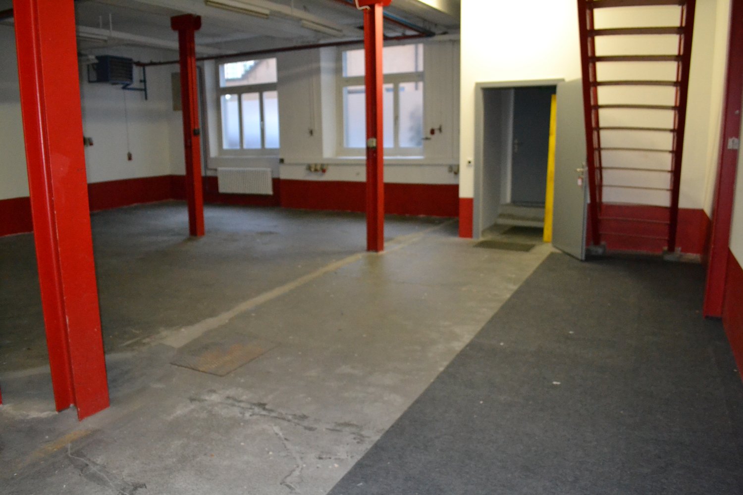 Empty room with red pillars, white walls, windows, radiator, open door, and a ladder.