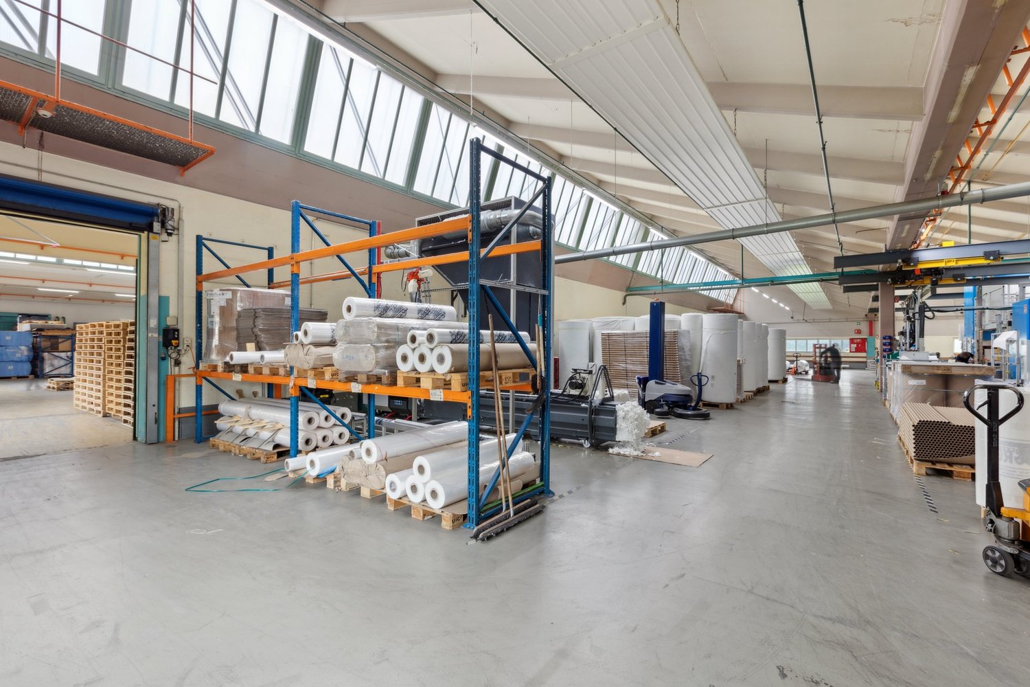 Large industrial warehouse with high ceilings, storage racks, and various materials and equipment stored on the premises. The space appears to be used for storage and distribution of goods.