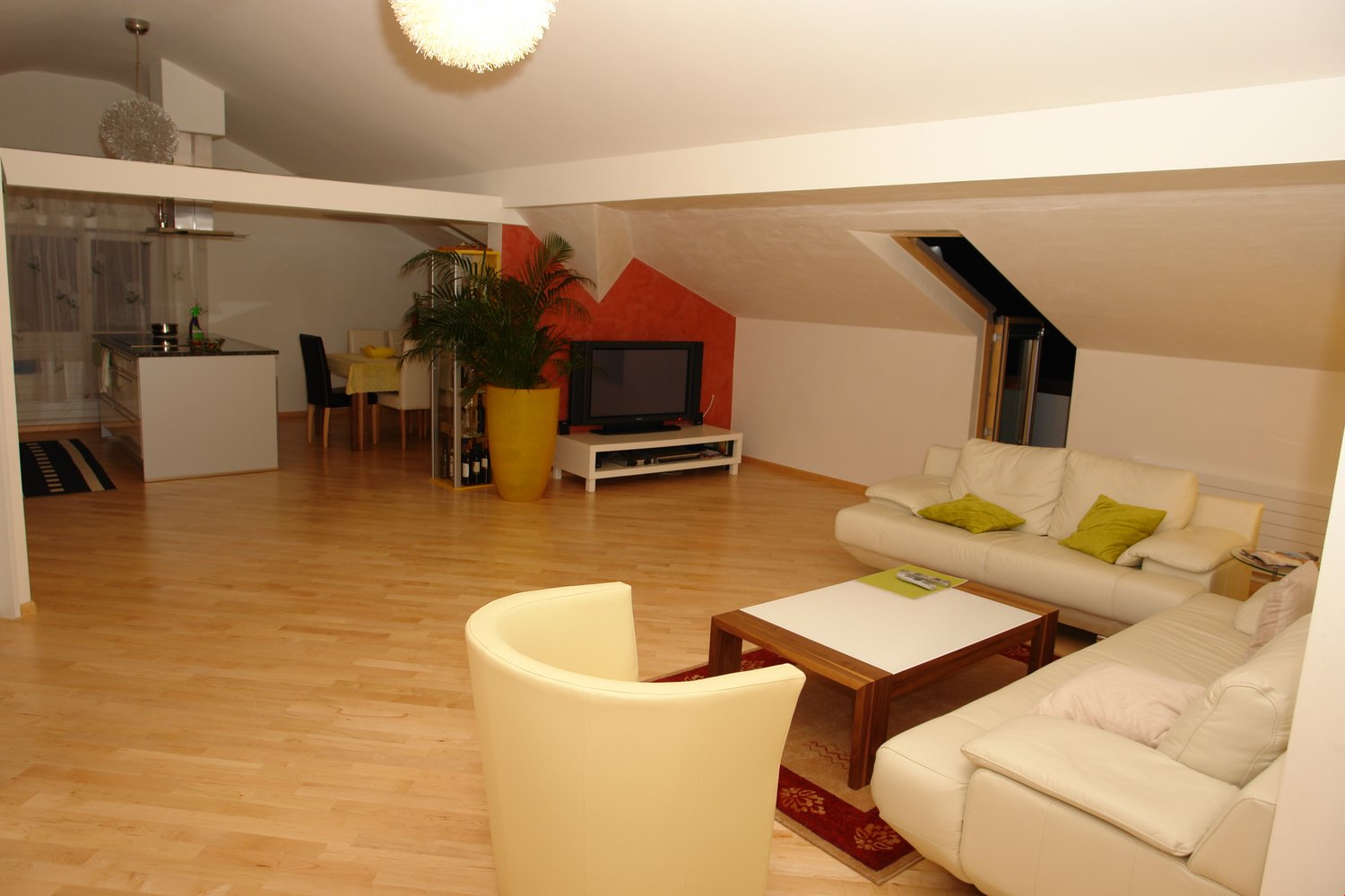 white leather couches, wooden coffee table, TV, potted plant, wooden floor, dining table and chairs, kitchen area