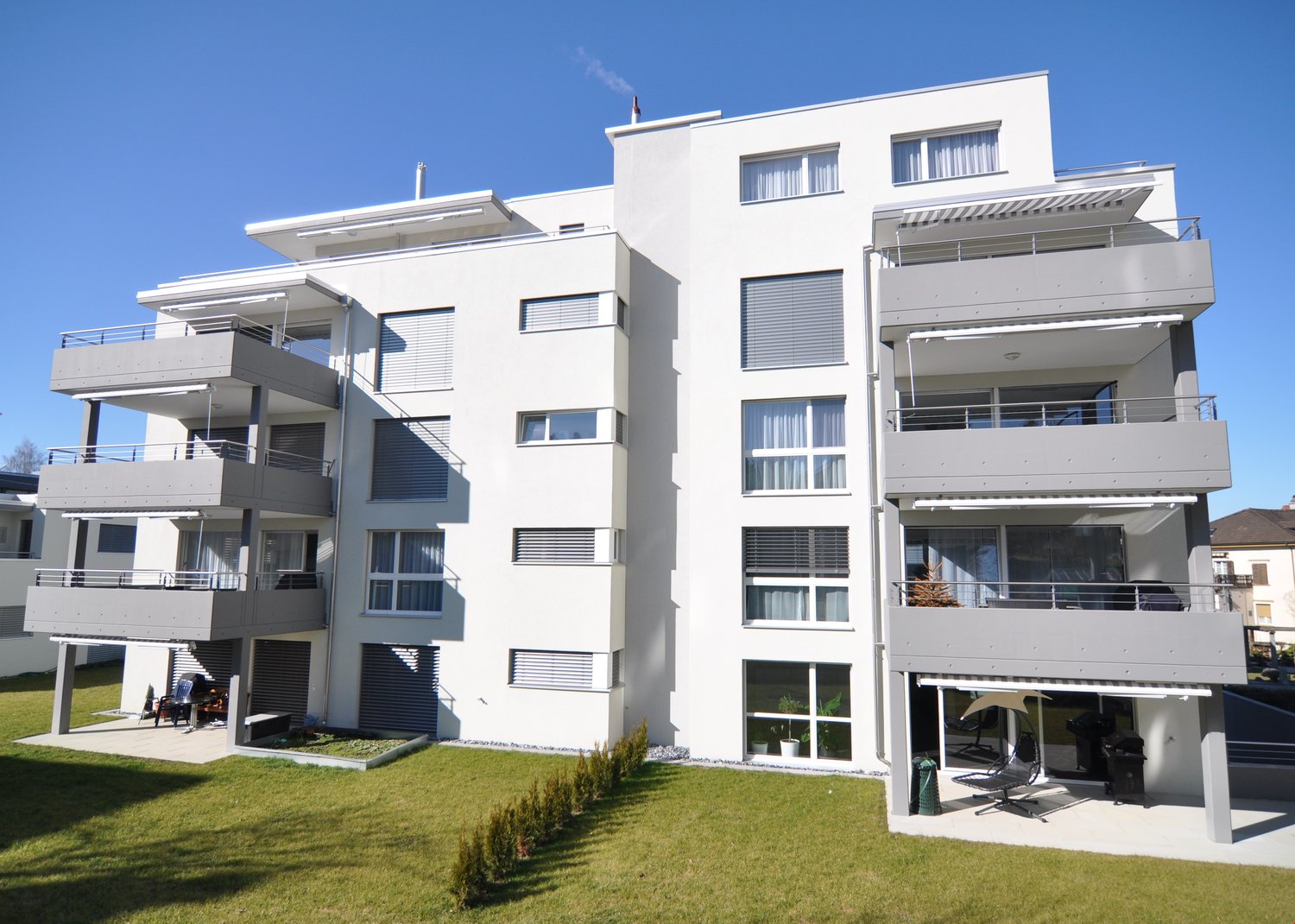 modern white building, 4 floors, balcony on each floor, green lawn in front, clear blue sky
