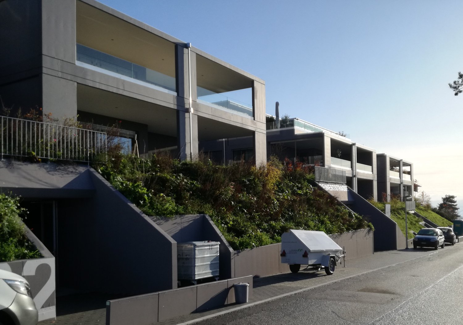 Multi-story modern building with balconies, glass windows, and a parking area in the foreground