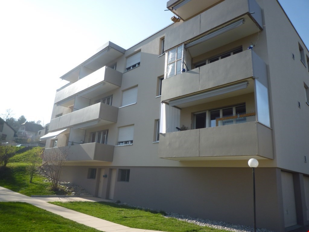 Multi-story apartment building with balconies, gray exterior, and landscaped grounds