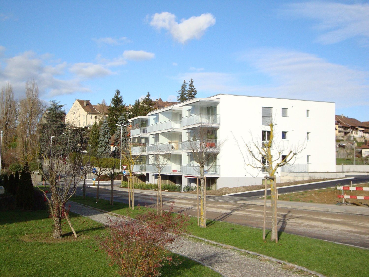 Modern white multi-story apartment building, with balconies, surrounded by trees and grass