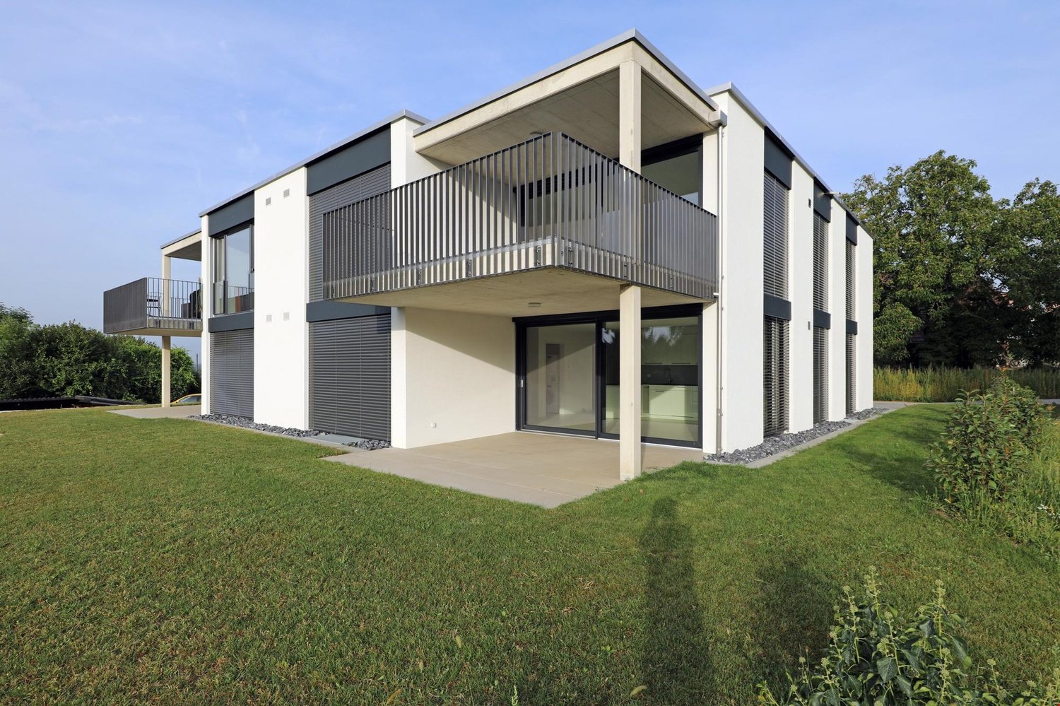 Modern house, white concrete exterior, glass doors and windows, two levels with balconies, spacious lawn in front