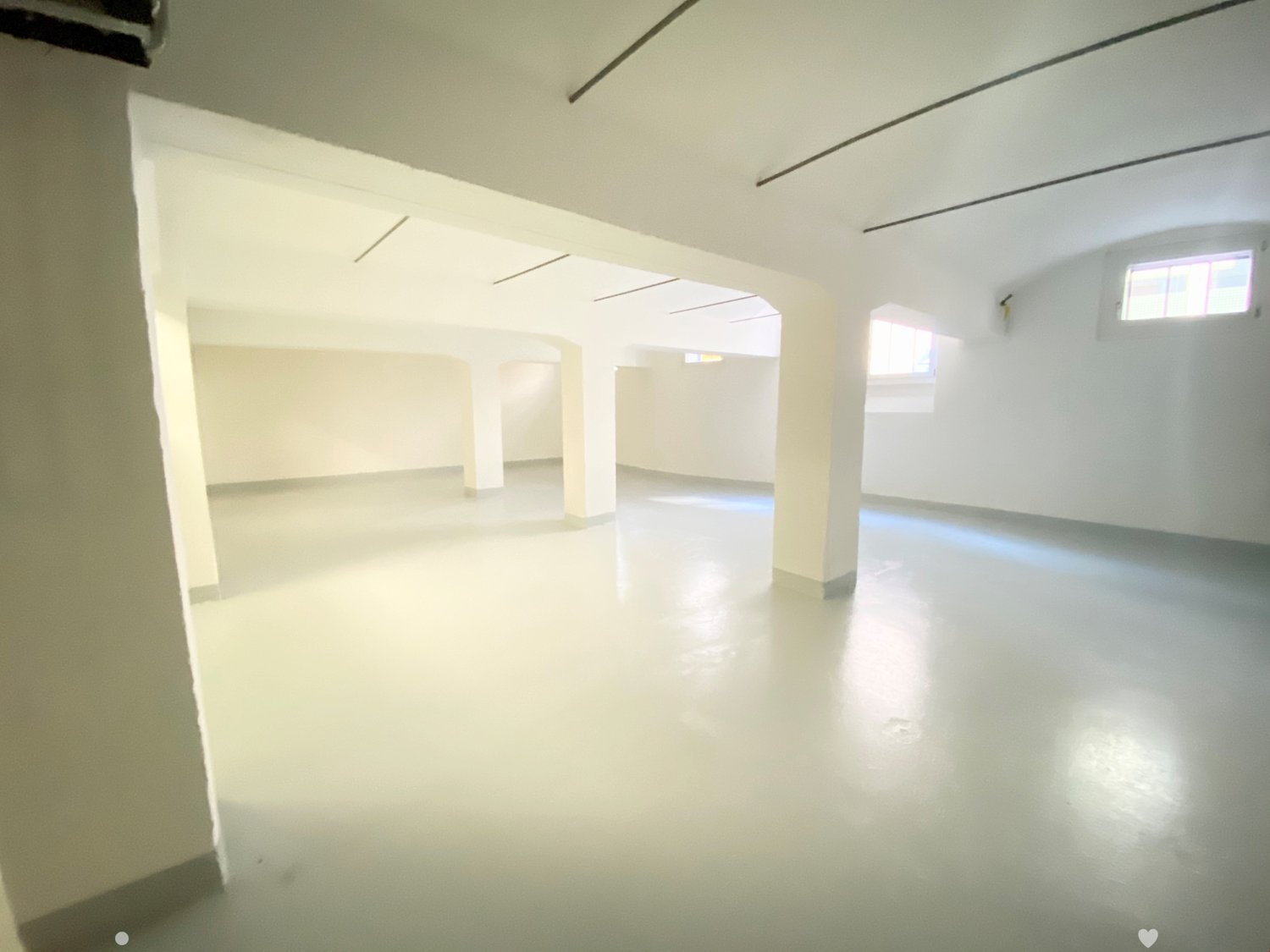 Large open space with white walls, concrete floor, and several windows providing natural light. The room appears to be an empty, unfinished space, possibly a loft or studio apartment.