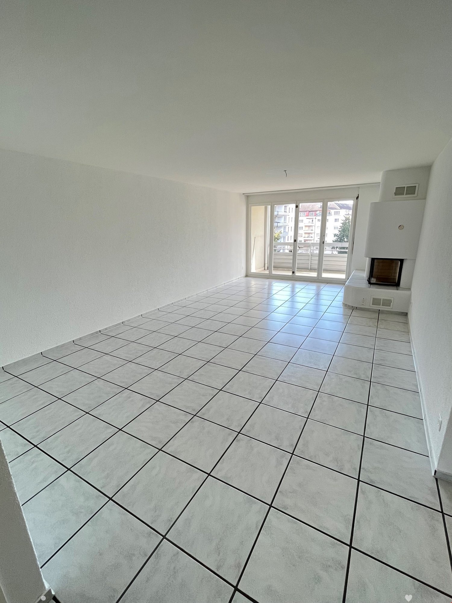 Spacious living room with large windows, tiled flooring, and a fireplace.
