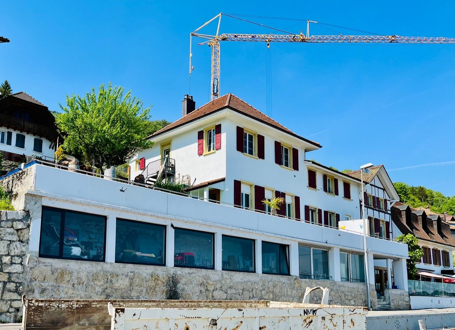 Two-story house, white with red shutters, stone wall, crane on top, balconies, windows with view