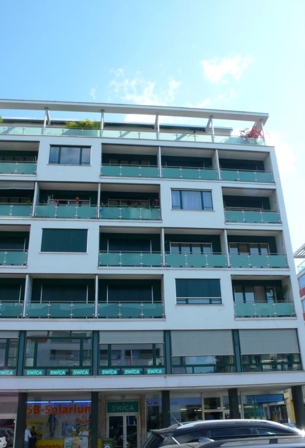 Modern apartment building, white paint, green frames, many balconies, ground floor commercial space