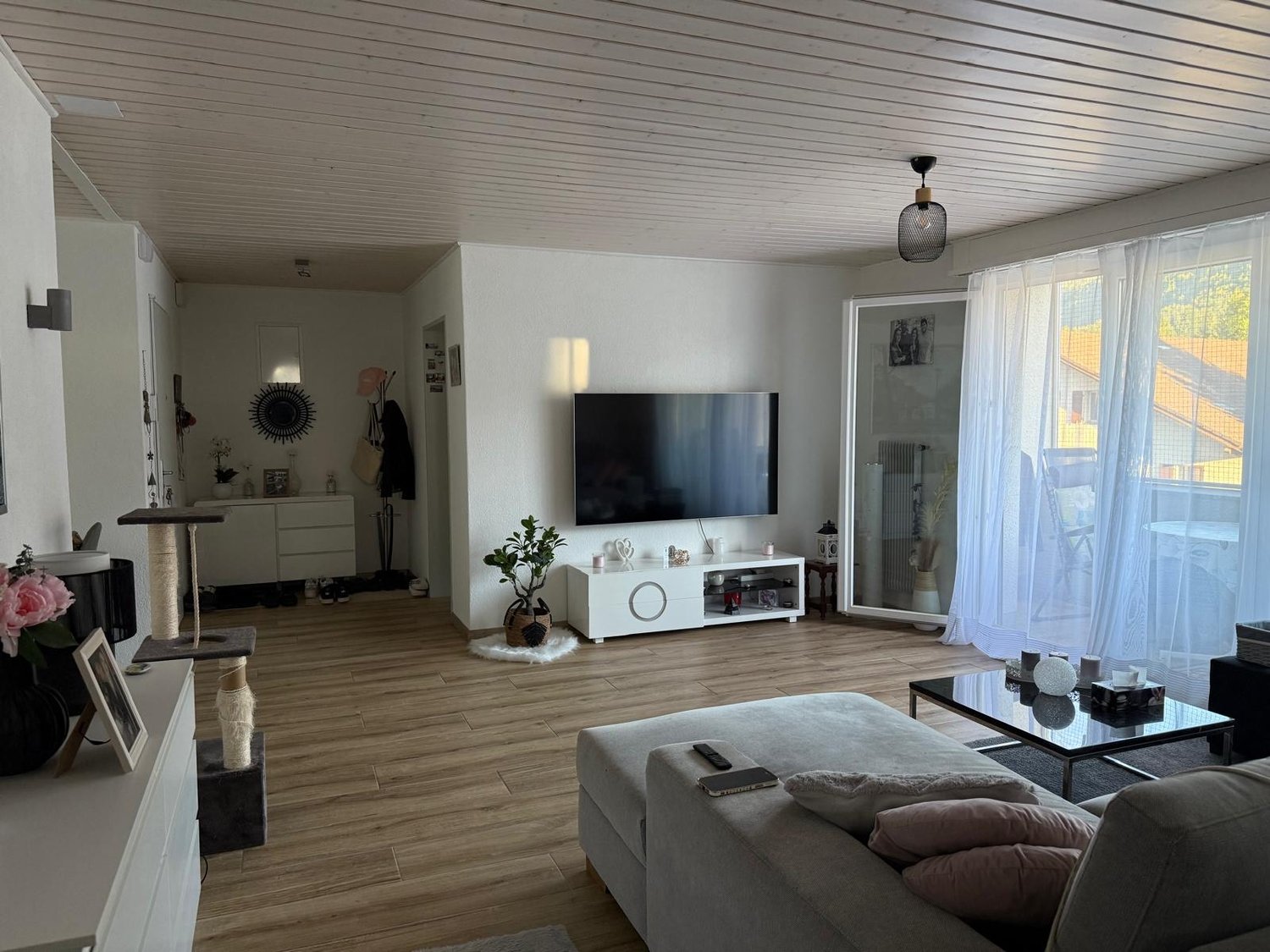 living room, flat screen tv, white shelves, wooden floor, couch with pillows, glass coffee table