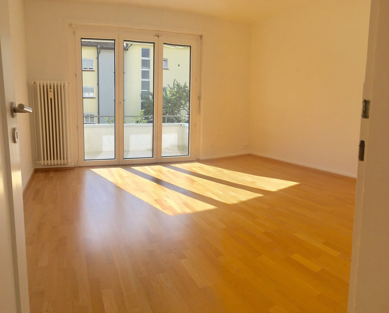 empty room, large glass doors leading to balcony, wooden floors, white walls