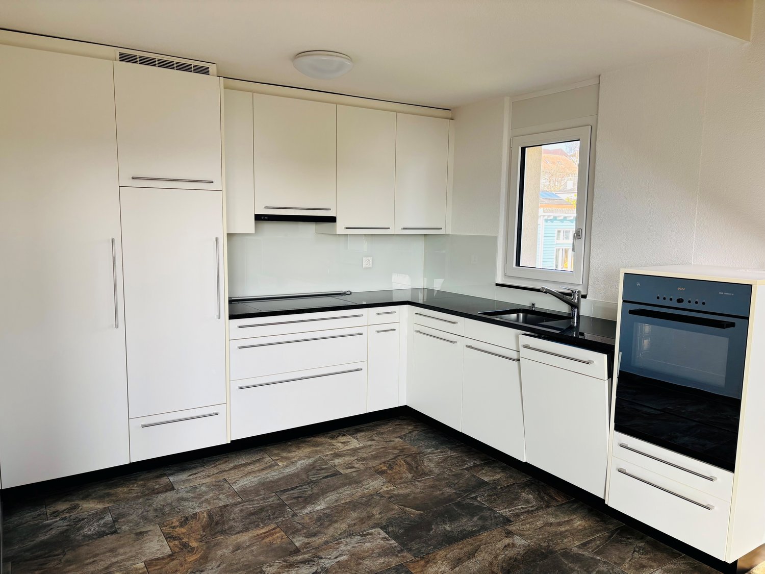 modern kitchen with white cabinets, black countertops, integrated appliances, natural light from a window