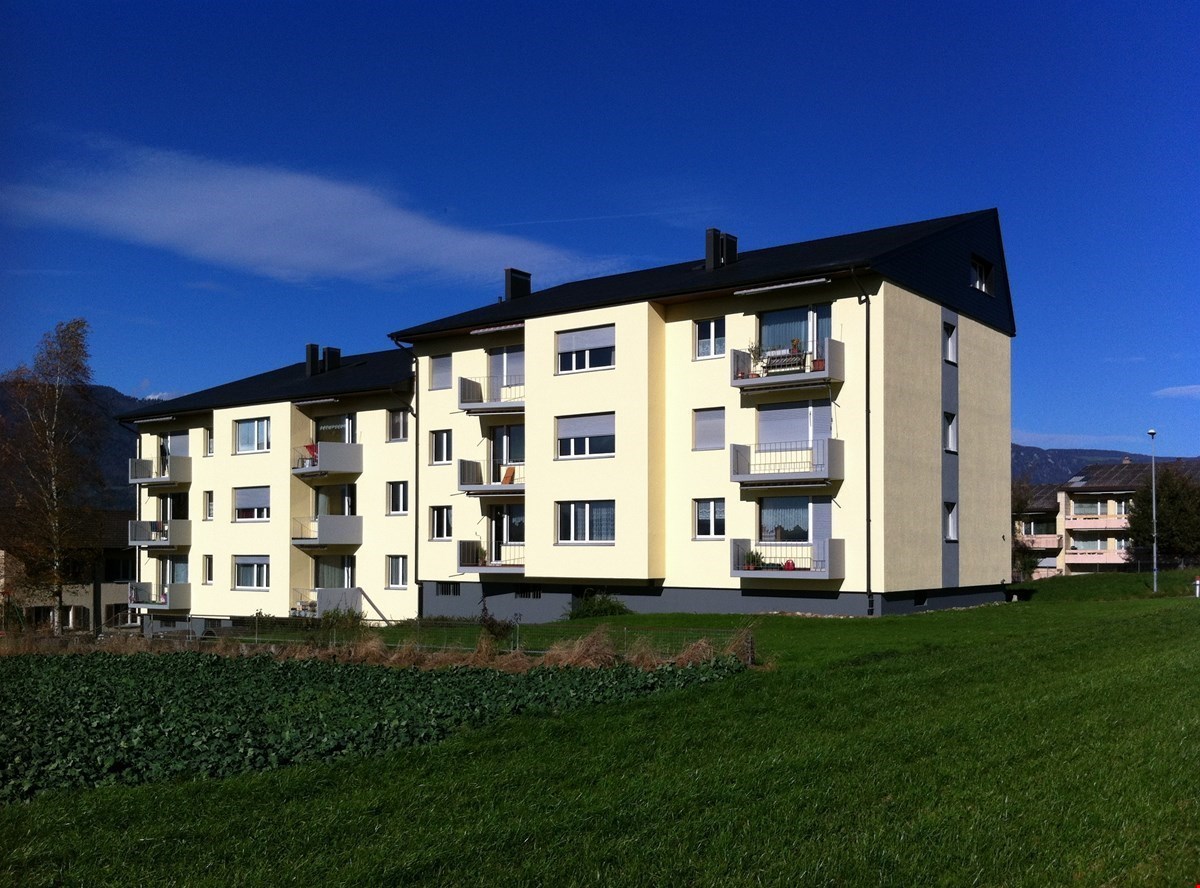 apartment building, multiple terraces, multiple stories, yellow exterior, black roofs, large green field