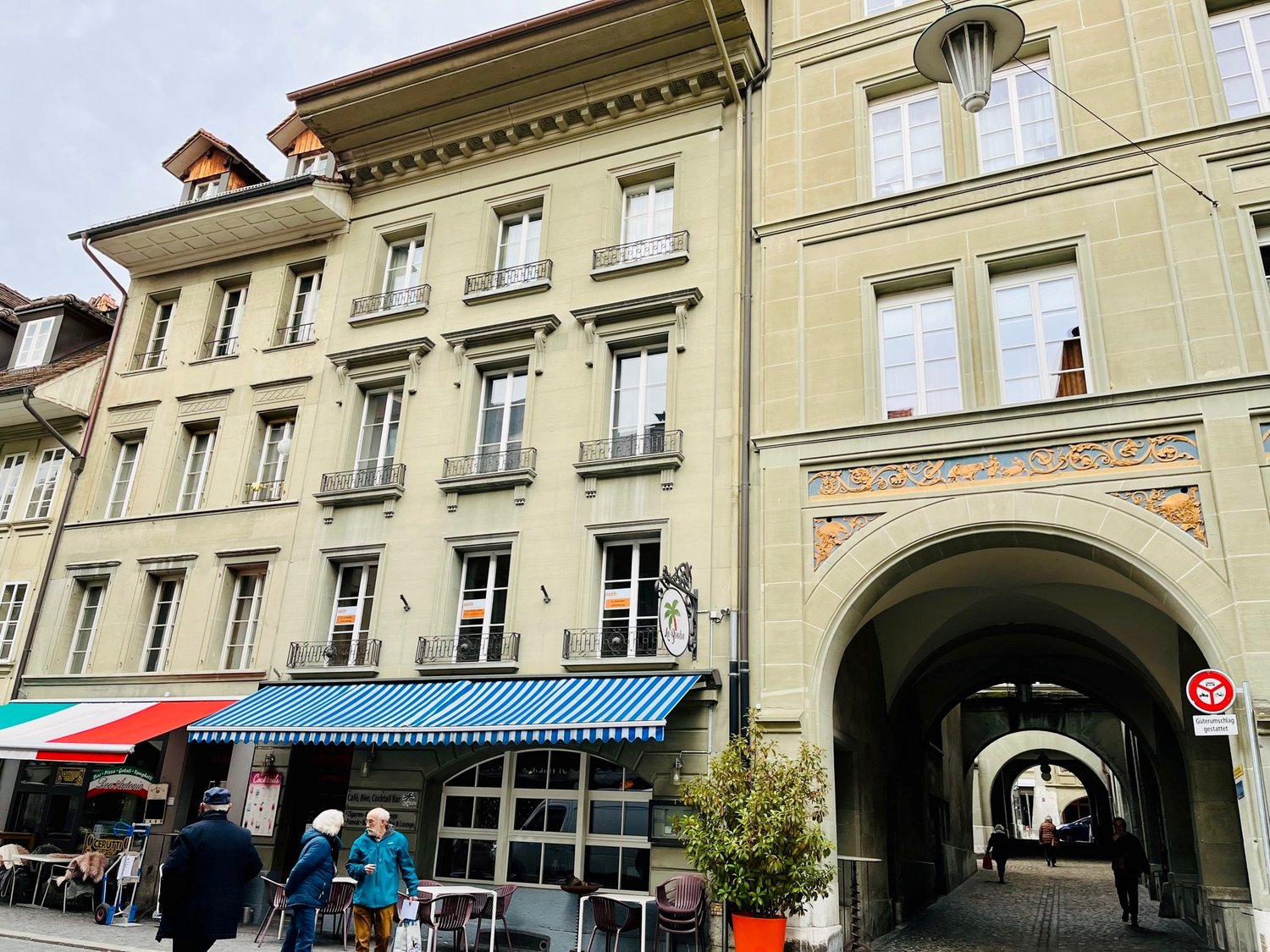 an apartment building with multiple balconies and windows, a cafe with a blue and white awning, and a street light