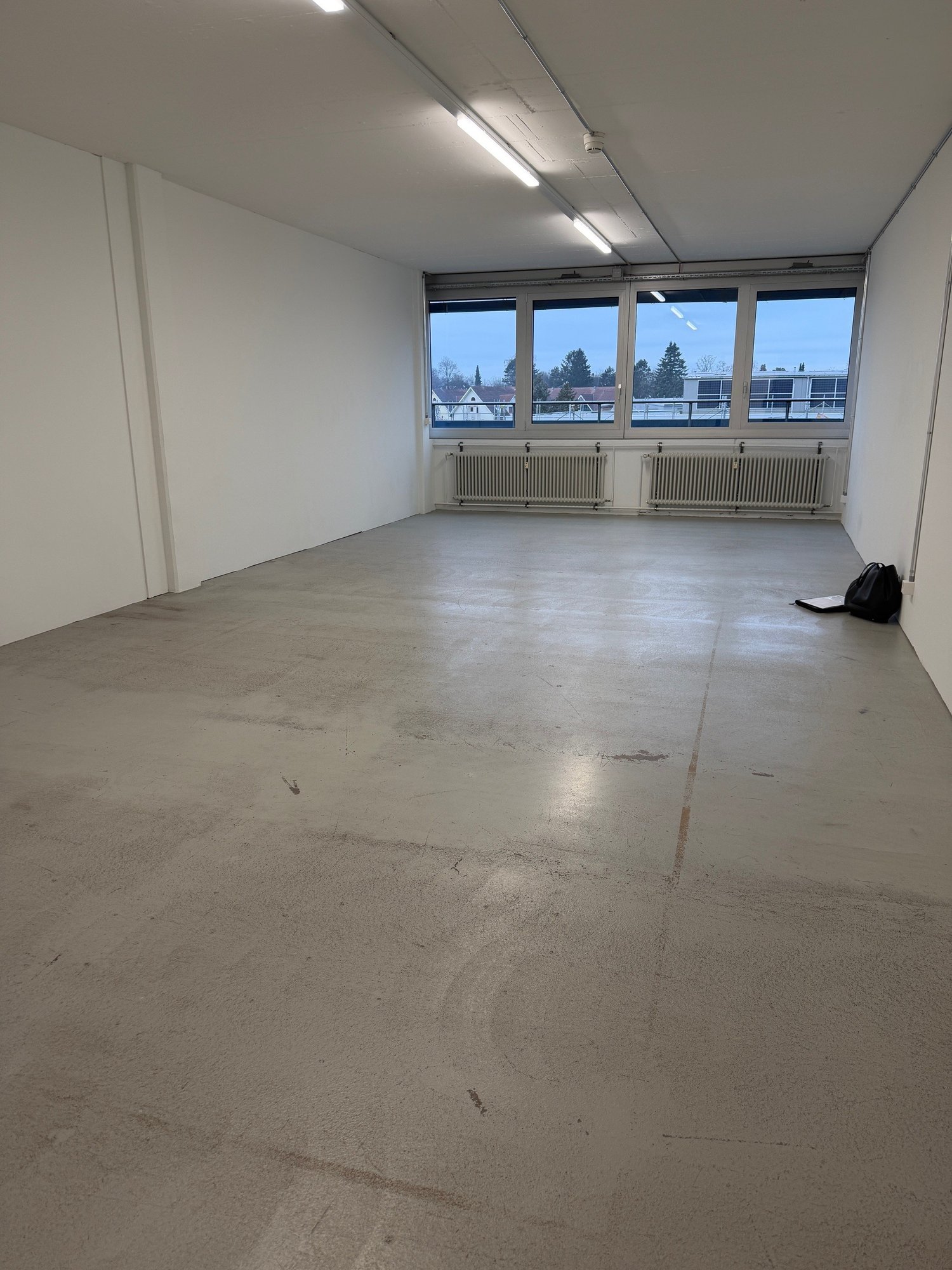 empty room with windows, concrete floor, mounted lights, radiators, white walls