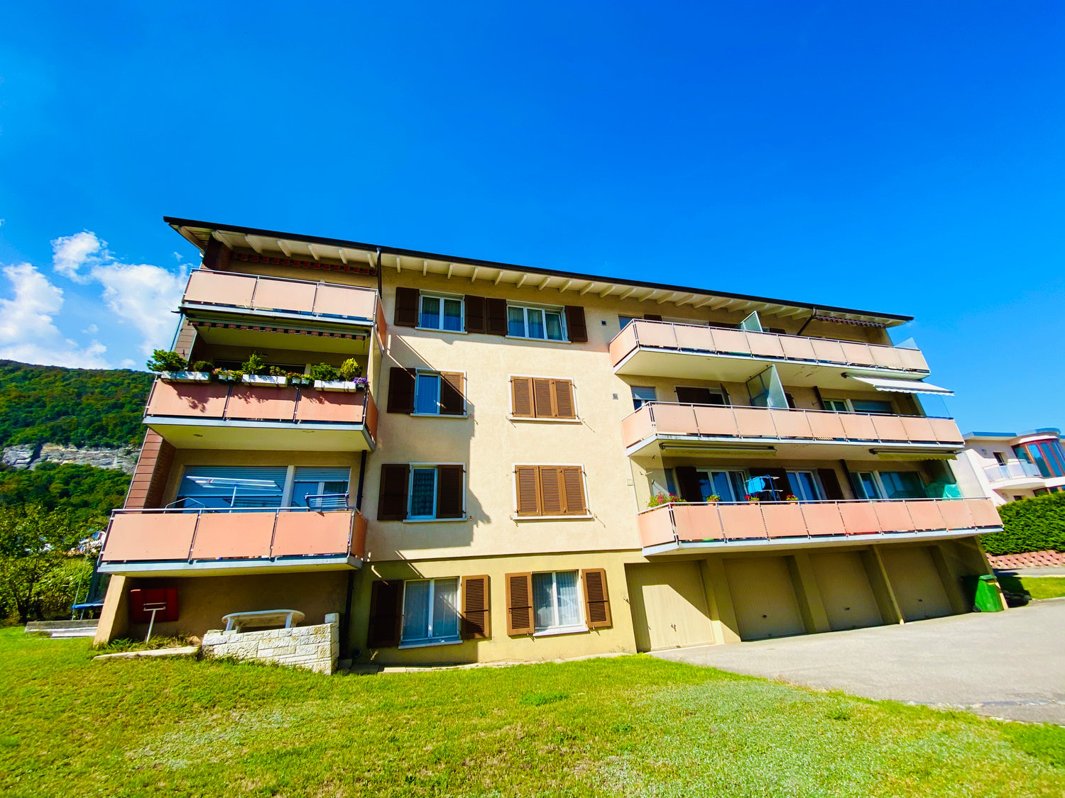 4 story apartment building, beige exterior, multiple balconies, garage, green lawn