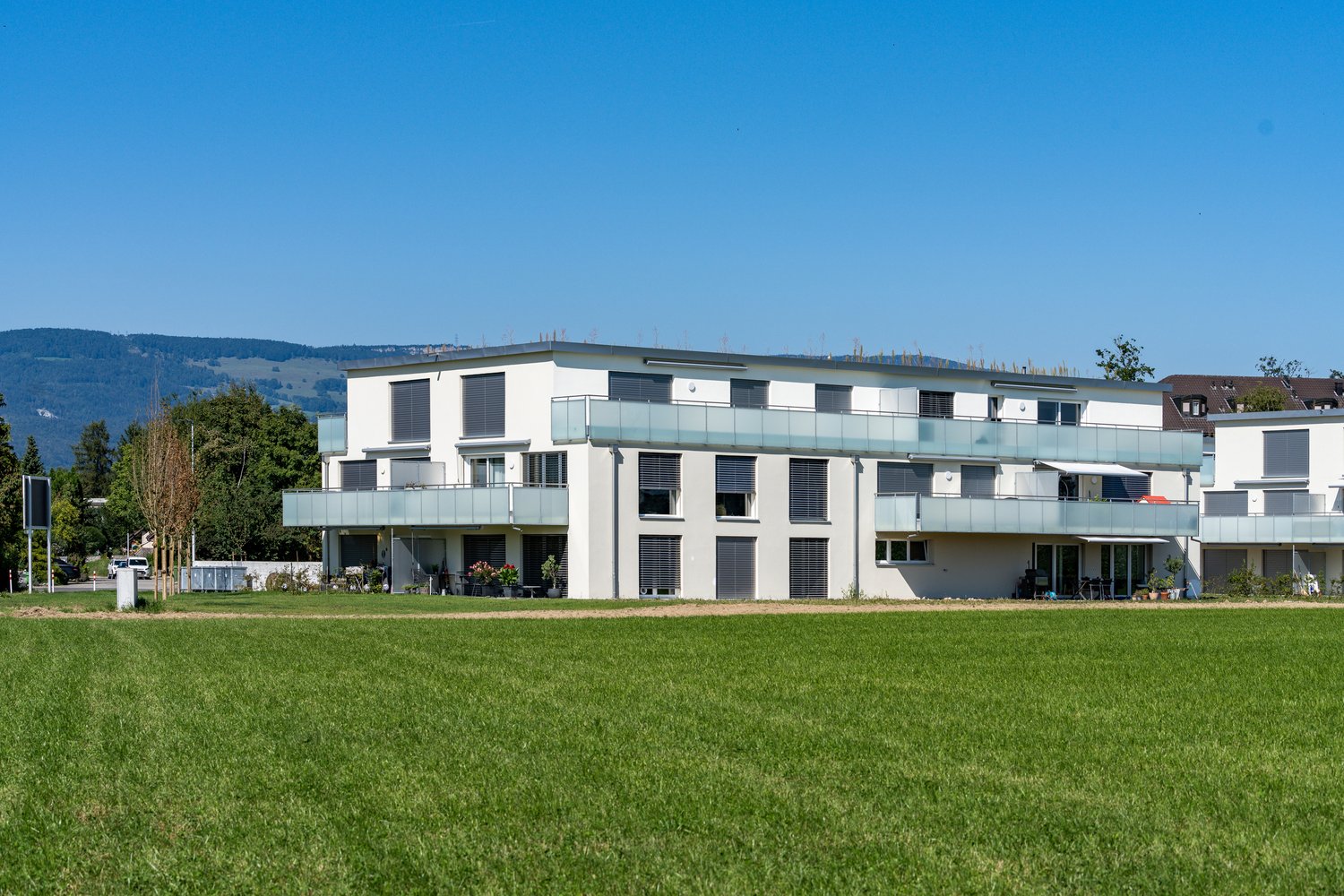 modern white building, balconies, garden, wide field in front