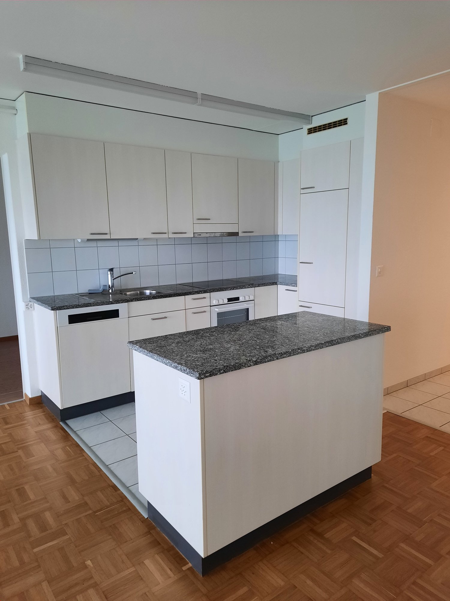 Modern kitchen with white cabinets, granite countertops, built-in appliances including a dishwasher, and hardwood flooring.