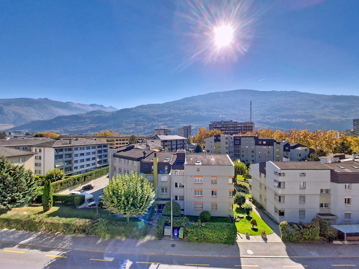 Apartment complex with multiple floors, greenery, and mountain views in the background