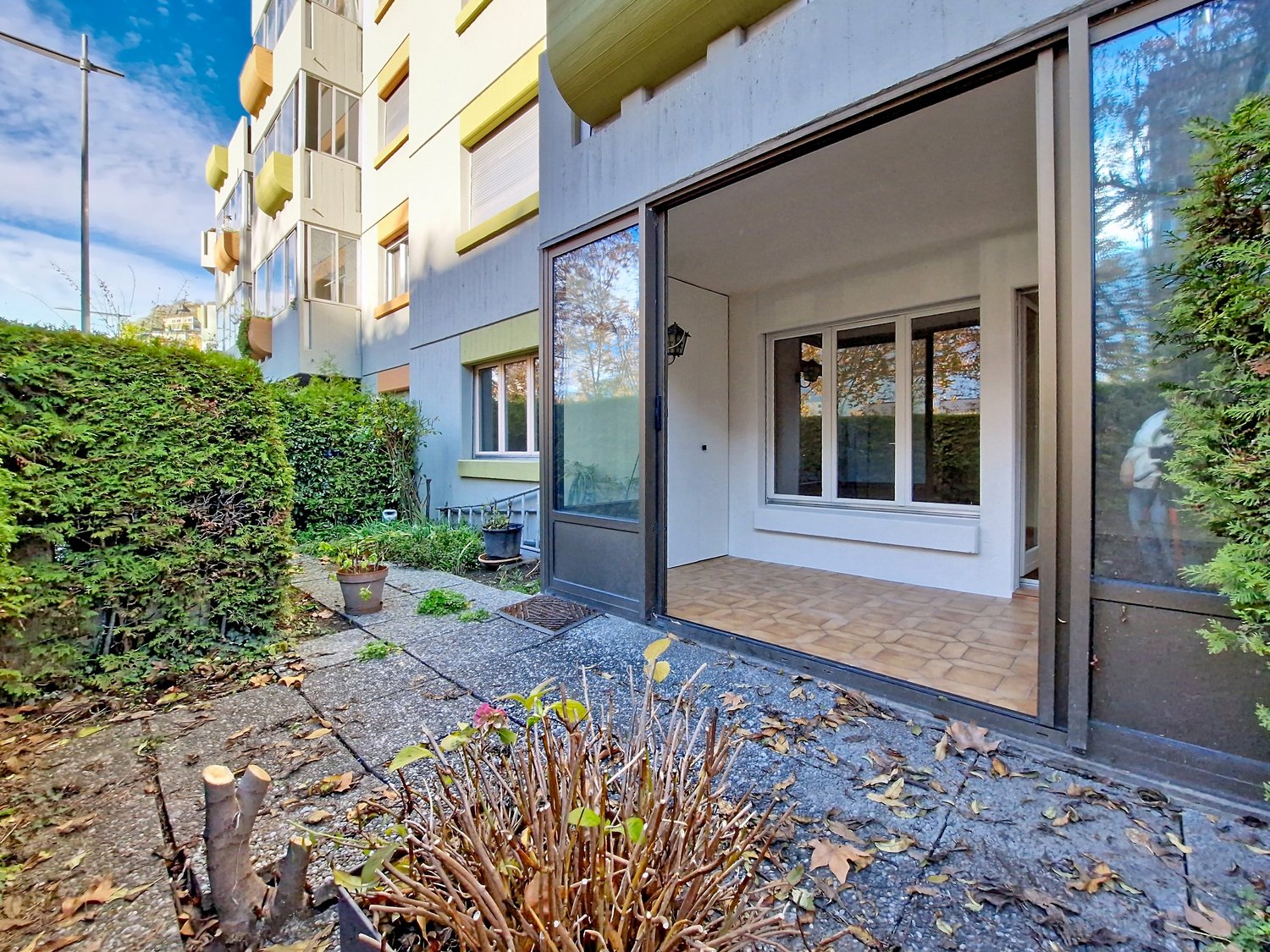 entrance to an apartment building, tile floor, potted plants, glass doors, small garden