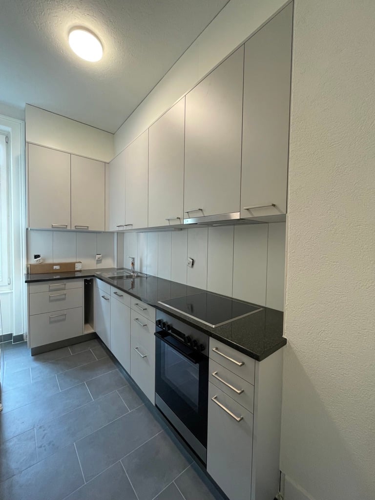 Modern kitchen with grey cabinets, black countertops, built-in oven, and dishwasher