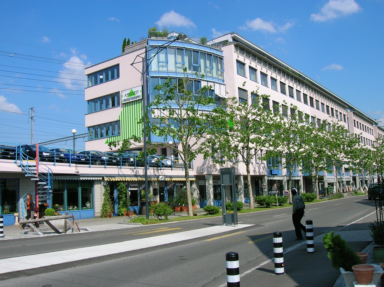 A multi-story building with a rooftop terrace, multiple windows, and a car parking area on the first floor.