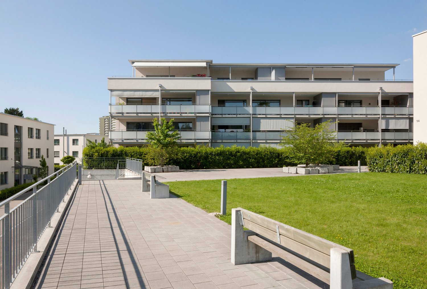 residential building with several balconies, concrete pathways, grass lawn, concrete benches, metal railings