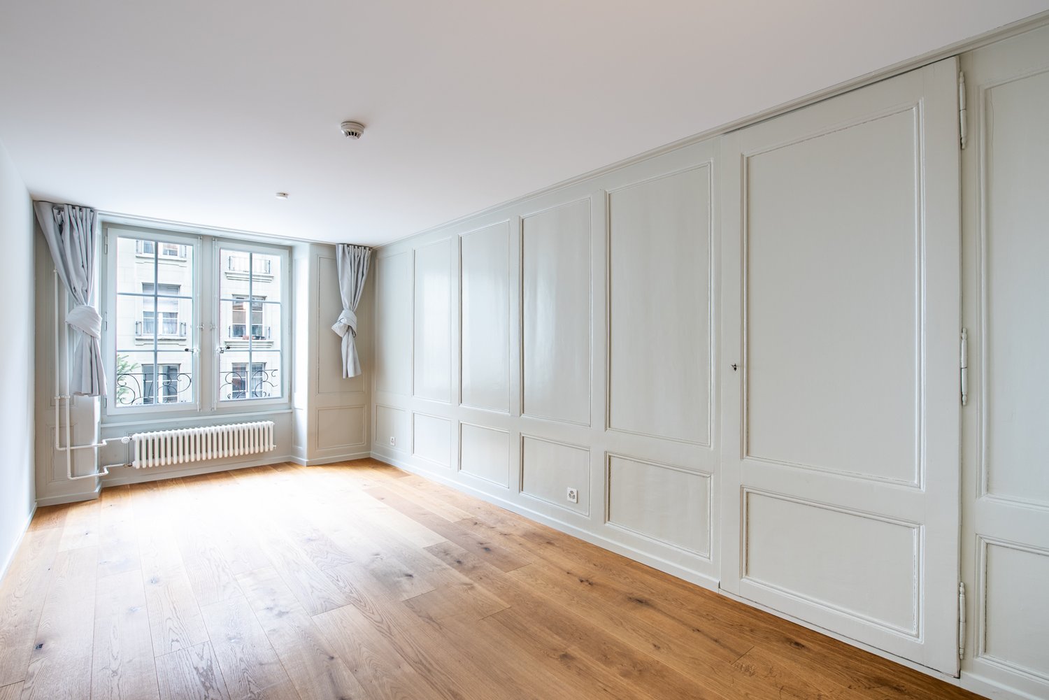 empty room, wooden floor, white walls, large windows, radiators, and curtains