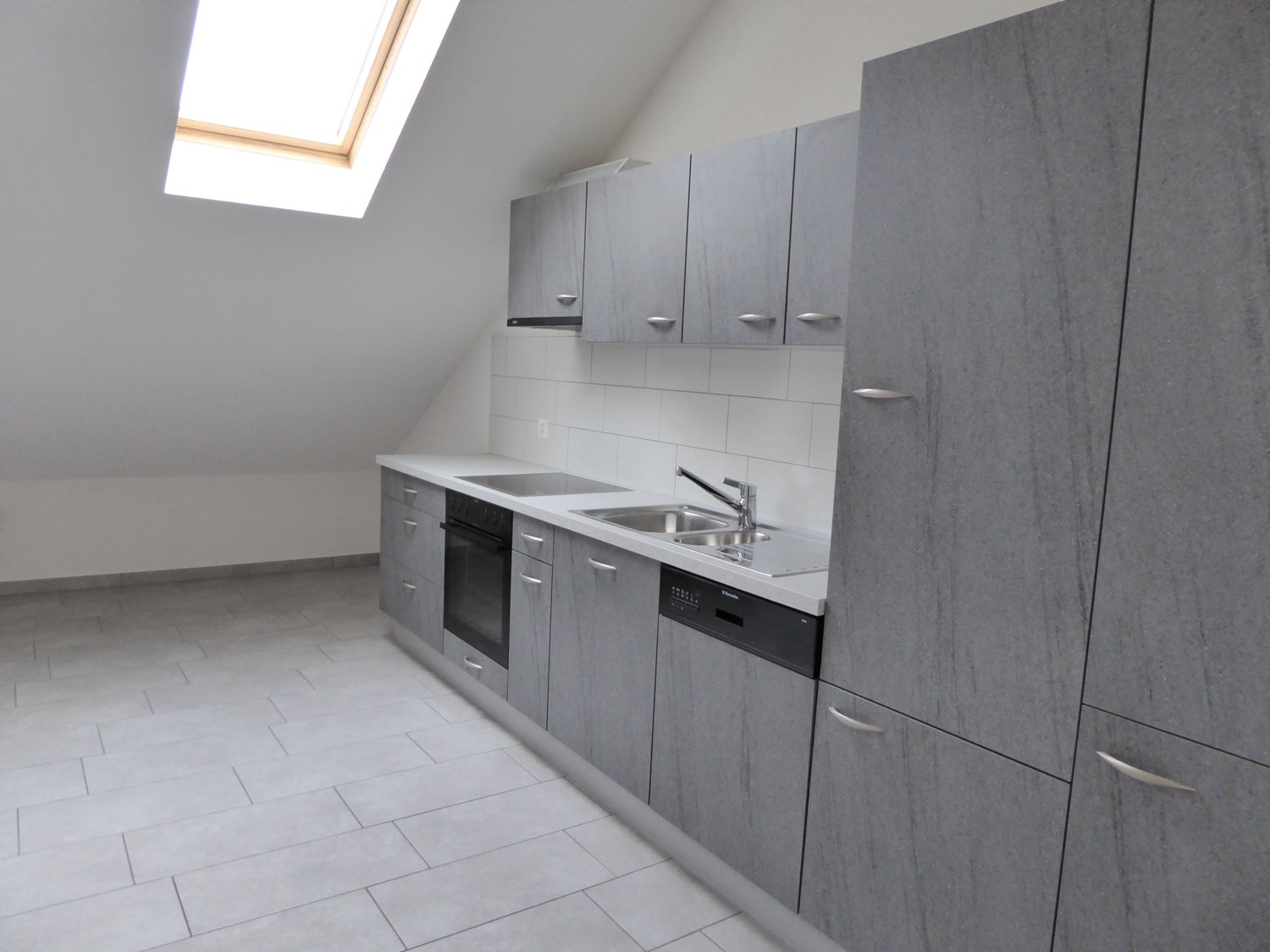 empty kitchen with light tile flooring, grey cabinets, stainless steel sink, dishwasher
