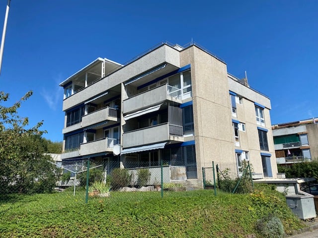 multi-storey building, concrete facade, balconies on upper floors, green fencing surrounding