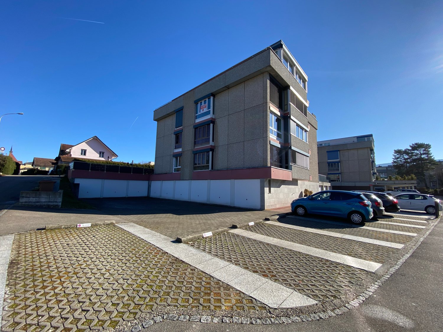 3-story building with multiple garages in front, white walls, cars parked in the front