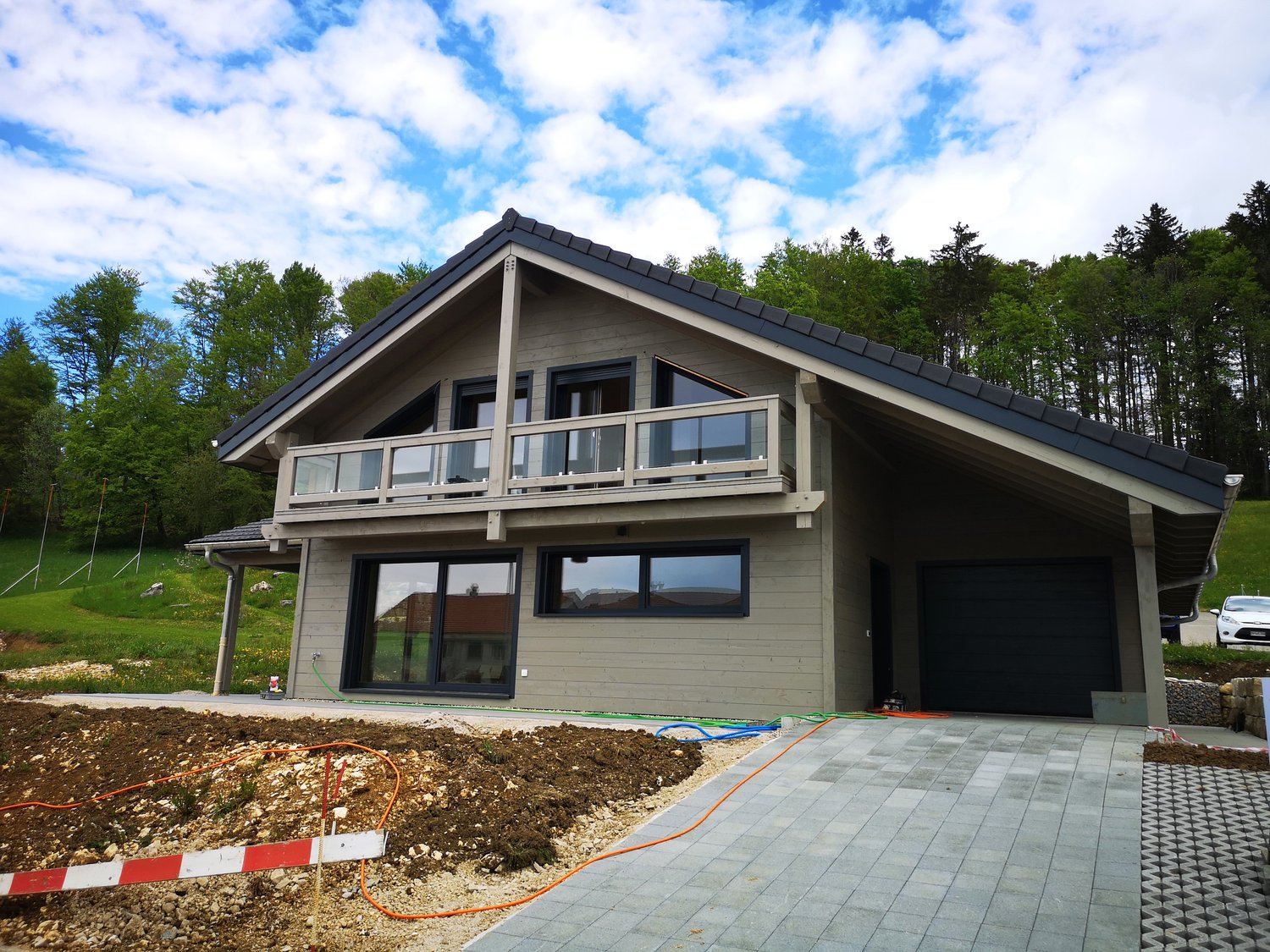Detached house with balcony, garage, modern design, located on a plot with green grass and trees in the background