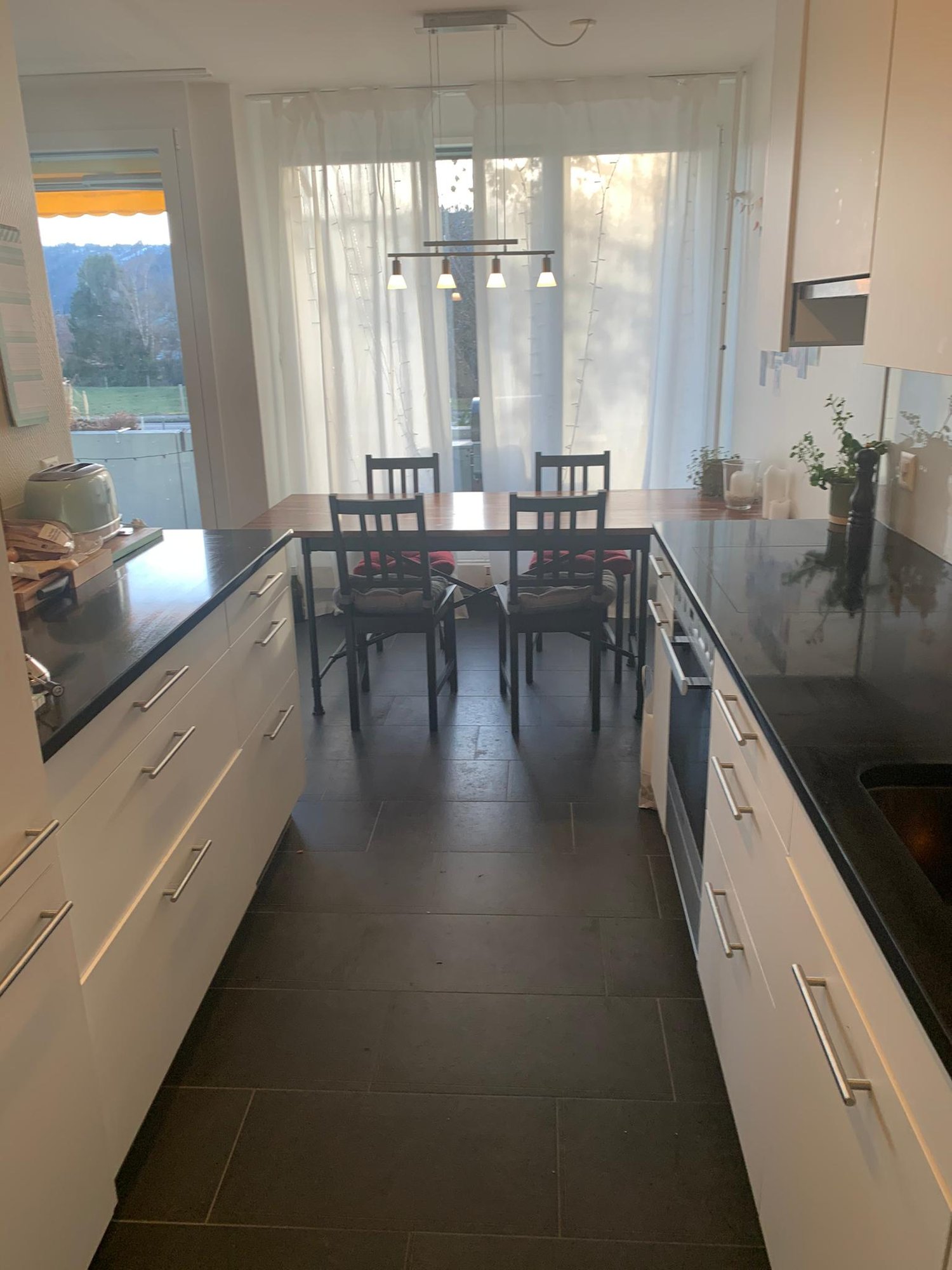 modern kitchen with dining area, wooden table, black floor, white cabinets, sliding glass doors