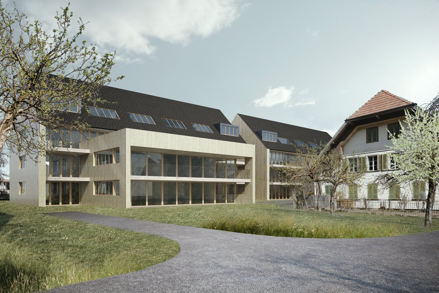 Multi-story building with a modern, glass-heavy design. The building has a flat roof and large windows, with balconies on some floors. The exterior is a mix of light-colored materials. The building is surrounded by a grassy area with trees.
