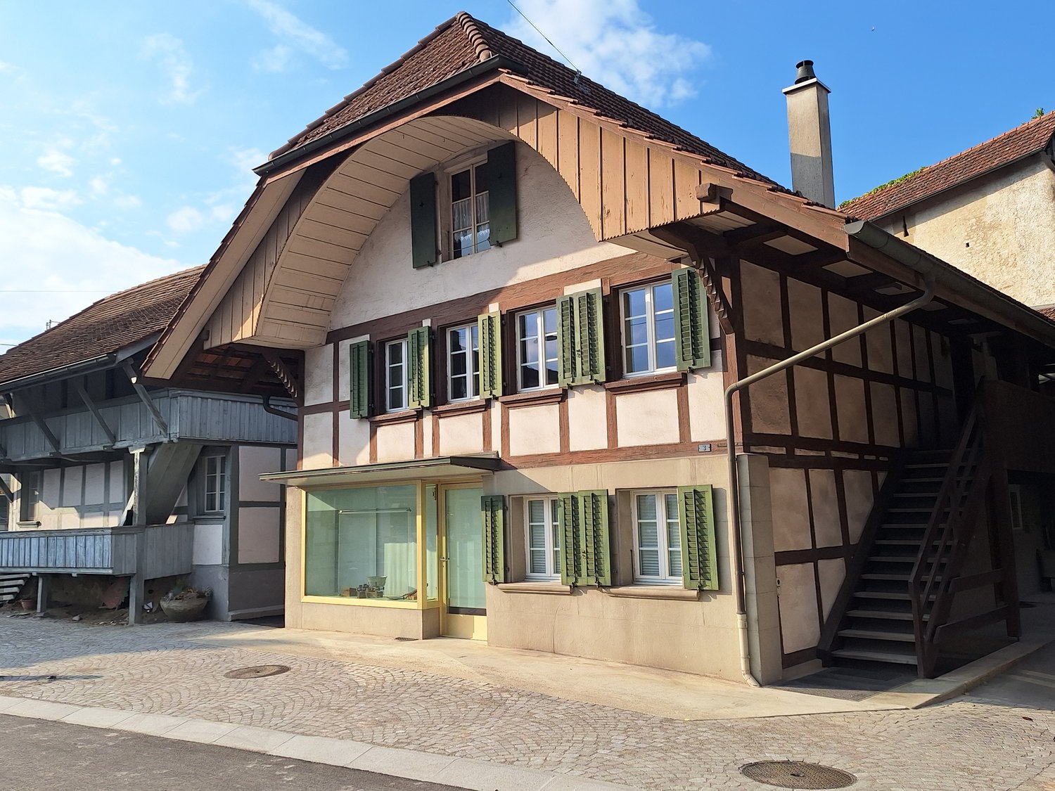 Traditional architectural building, wooden facade, green shutters, tiled roof, staircase, storefront window