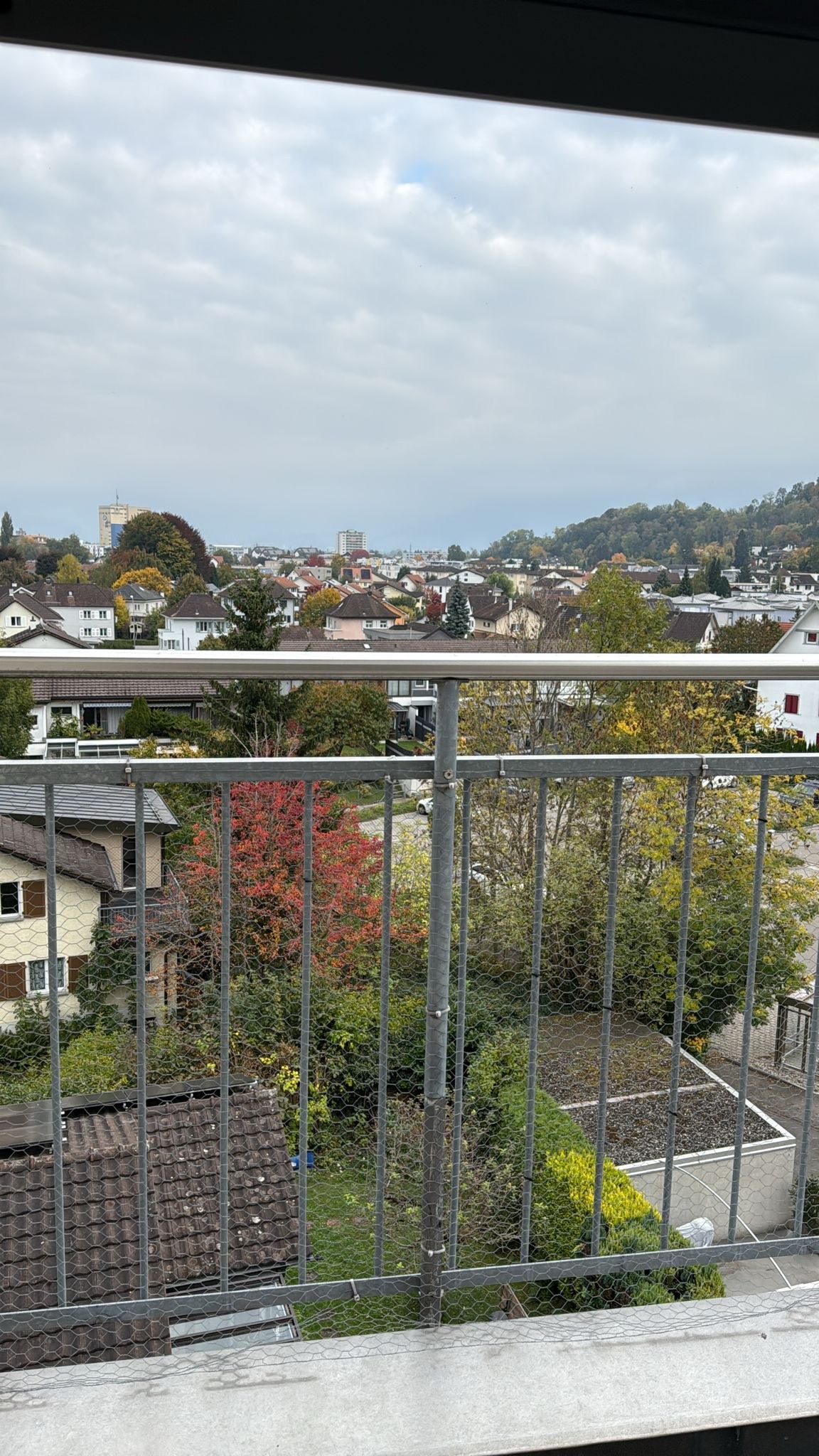 A balcony with railings, a tree in the foreground, distant houses, and a clear view of the cityscape.