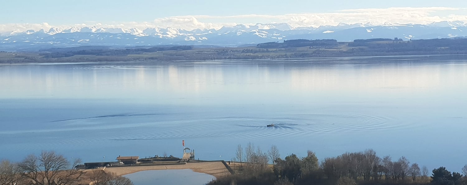 vast lake with clear blue water, mountain range in the background, small dock, ripples