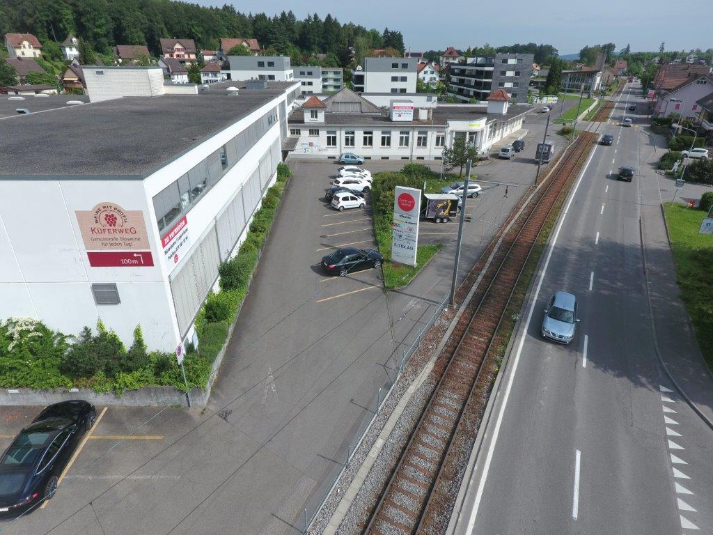 White building with signage, multiple cars parked in parking lot, road with vehicles