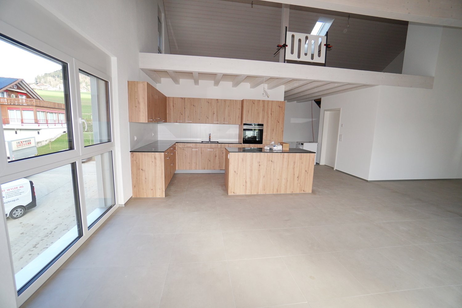 Open-concept kitchen with wooden cabinets, white countertops, and a dishwasher. Large windows provide natural light and a view of the surrounding landscape.