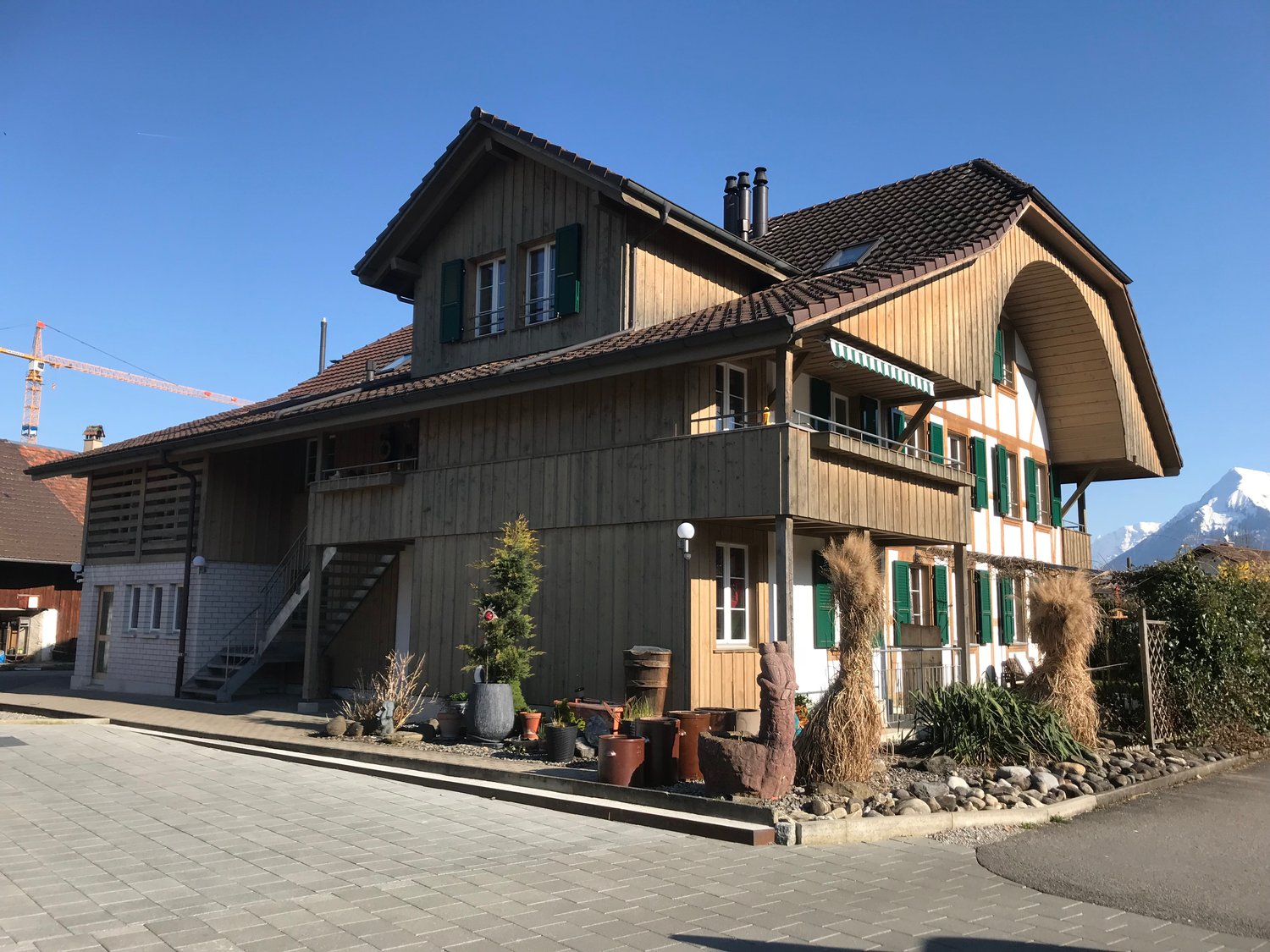 two-story chalet, wooden exterior, green shutters, balconies, surrounded by plants and rocks, mountain in the background