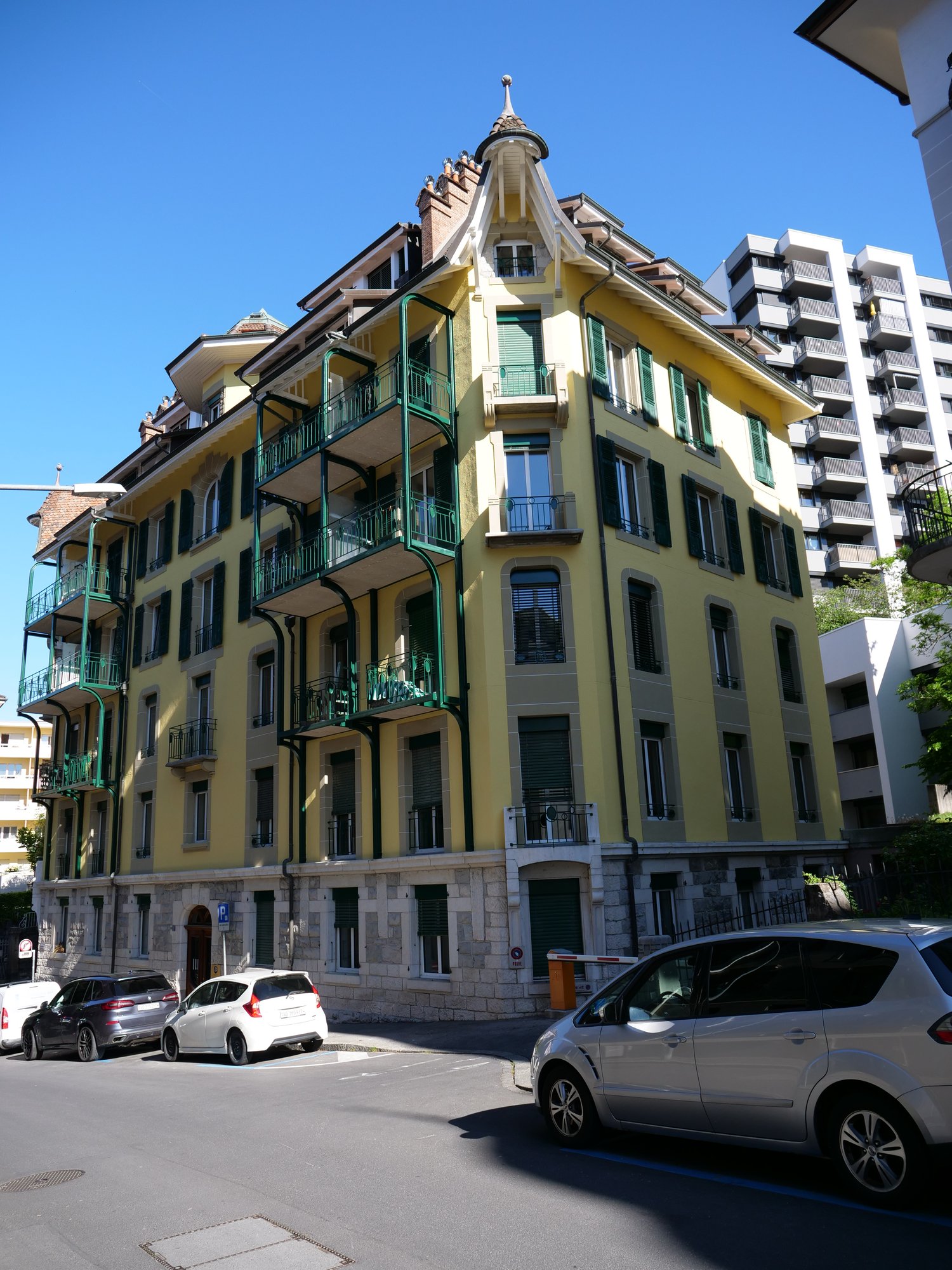 5 story building, yellow exterior, green balconies, multiple windows, stone base