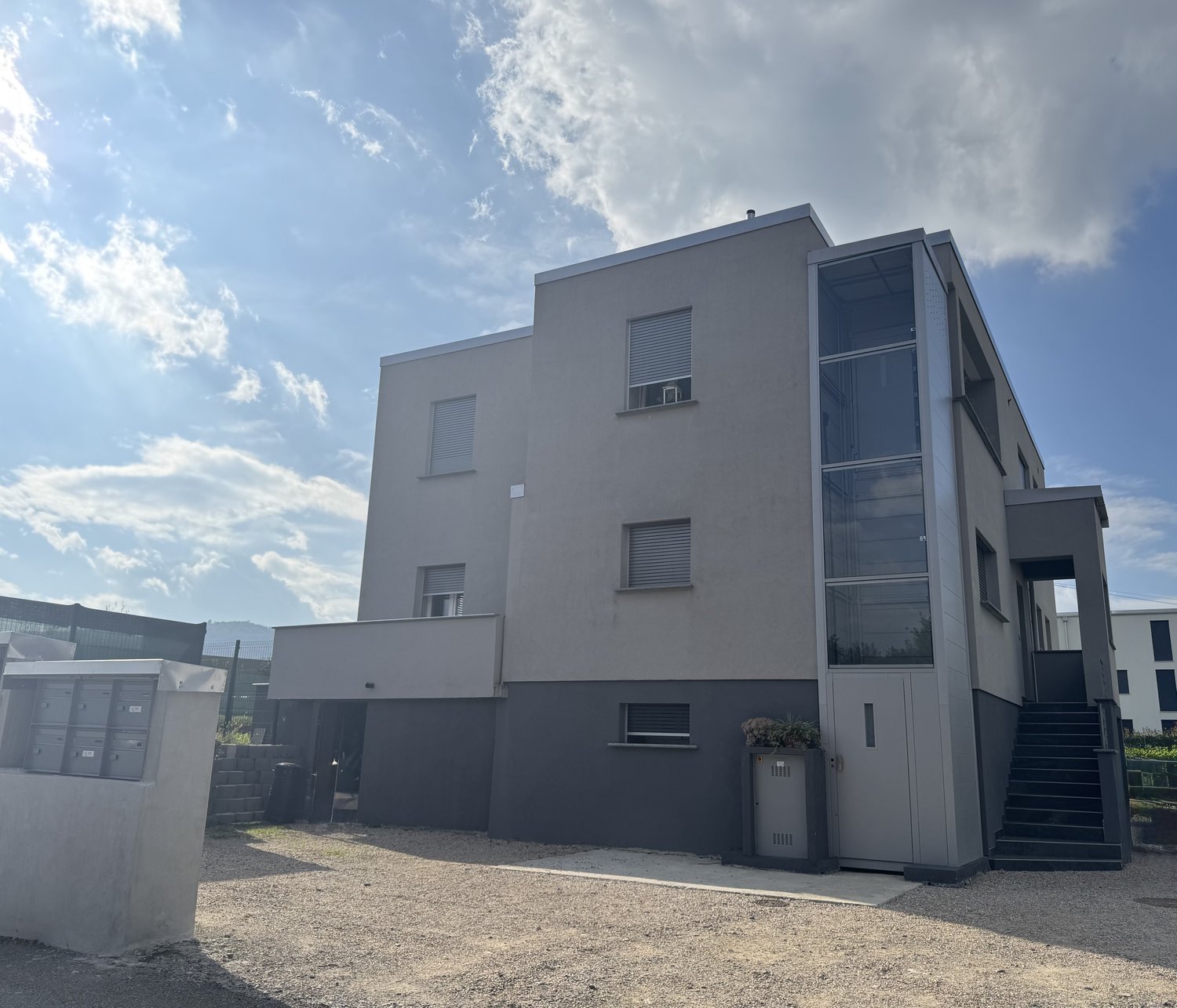 Modern apartment building, glass windows, grey walls, entrance door, small garden