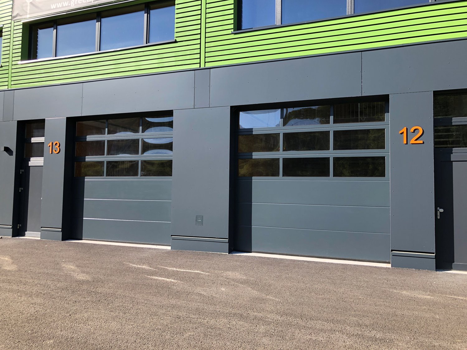2-story commercial building with green and gray exterior, large windows, and garage doors