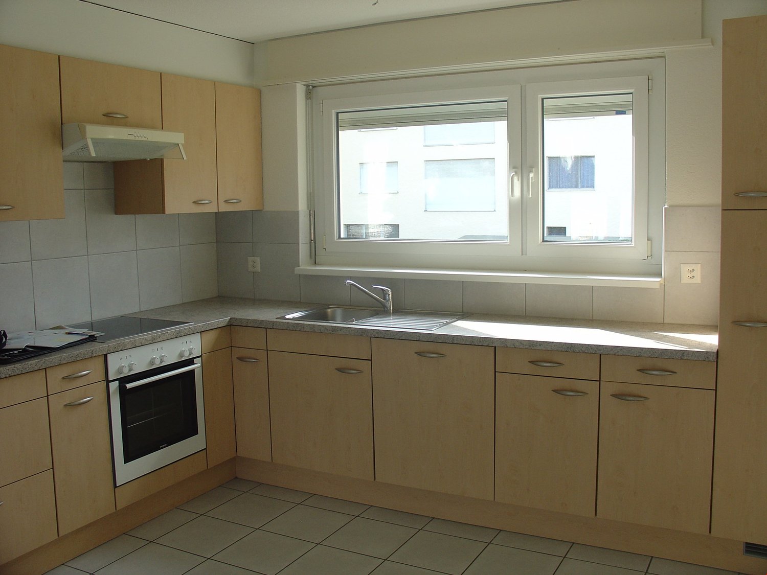 Spacious kitchen with light wood cabinets, granite countertops, stainless steel appliances including a dishwasher, and large windows providing natural light.