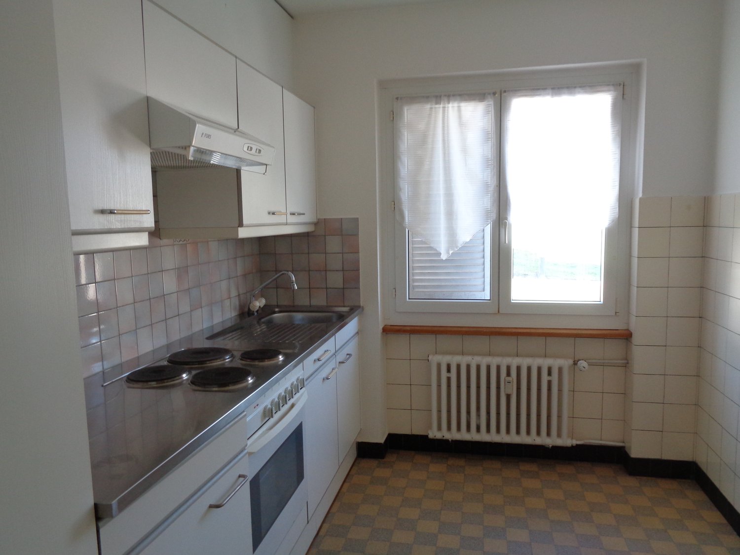 Compact kitchen with white cabinets, tiled backsplash, electric stove, dishwasher, and washing machine. The kitchen has a window providing natural light.