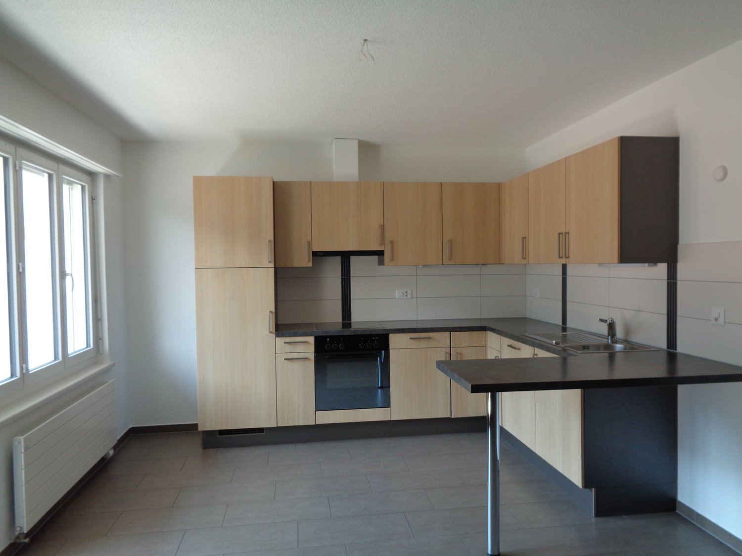 empty kitchen with island, white tile backsplash, wooden cabinets, black counter top, white walls, white appliances