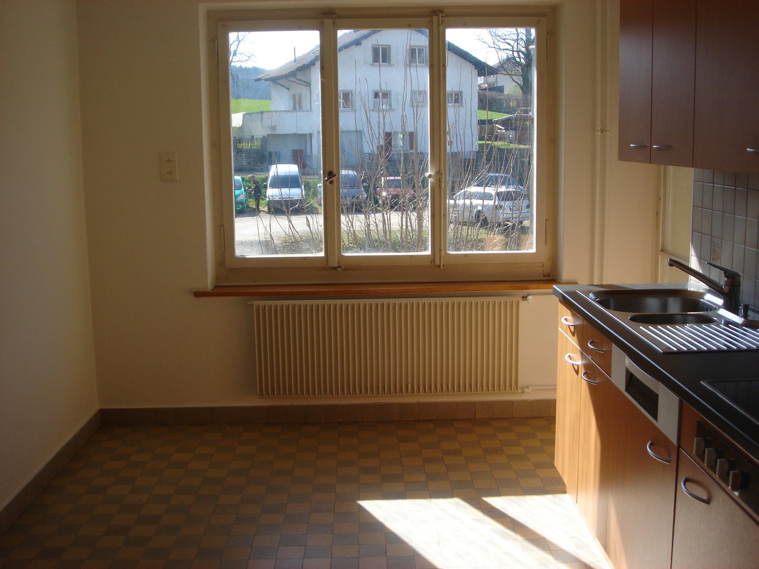empty kitchen with checkered floor, white walls, window, radiator, sink, faucet, cabinets, dishwasher