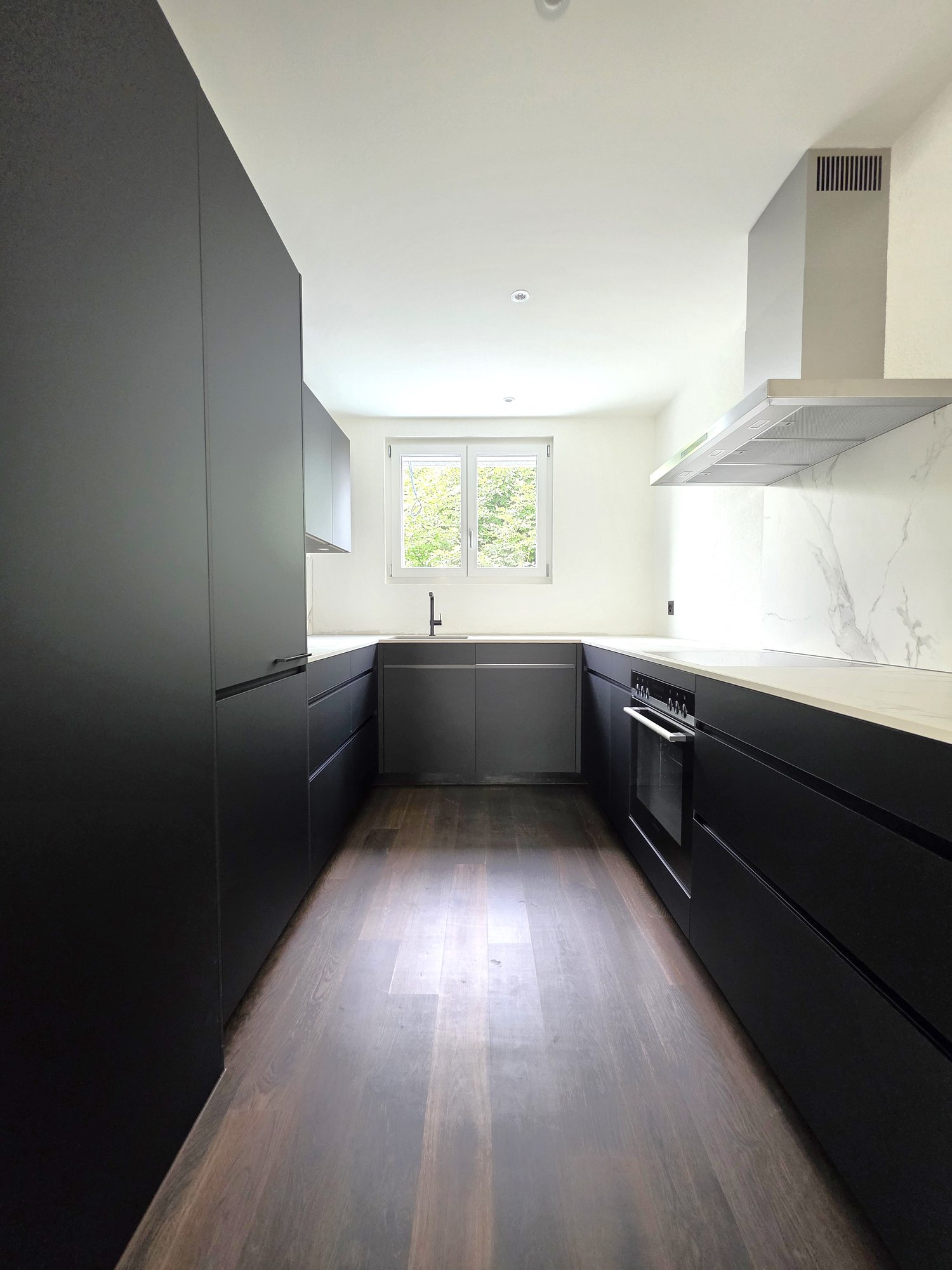 Modern kitchen with black cabinets, white countertops, stainless steel appliances, and a window overlooking the outdoors.