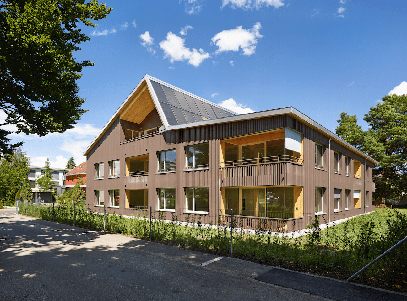 3 story building, brown exterior, solar panels on roof, multiple balconies, large windows